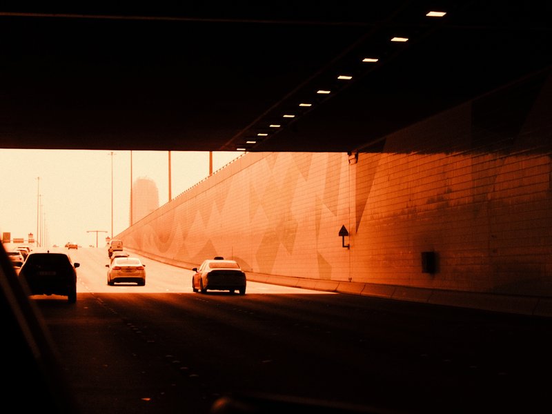 Cars exiting a tunnel into bright light with an orange hue, urban setting.
