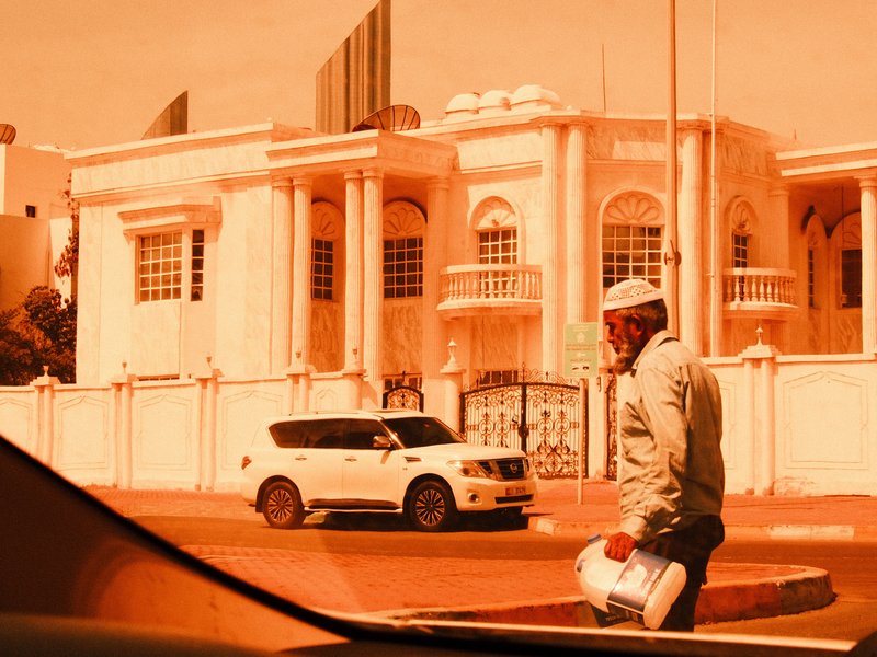 A man holding a megaphone walks past a large white building under an orange hue.