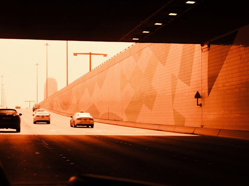 Cars driving through a tunnel with a warm orange hue and patterned wall.