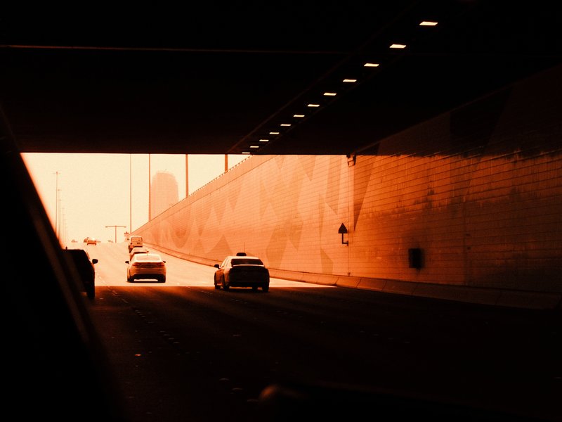 Cars exiting a tunnel into bright light, with warm orange tones and shadows on the walls.