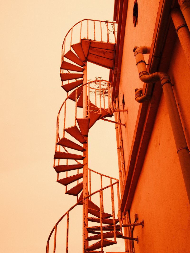 Spiral staircase against an orange sky, showcasing architectural details and textures.