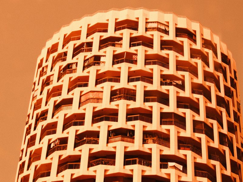 Close-up of a cylindrical building with a patterned facade against an orange sky.