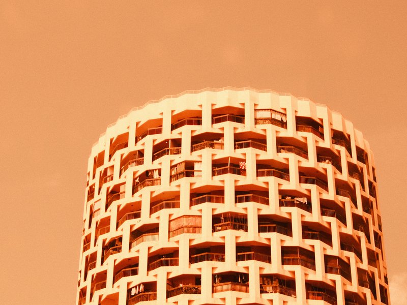 Close-up of a circular building with a grid-like facade against an orange sky.