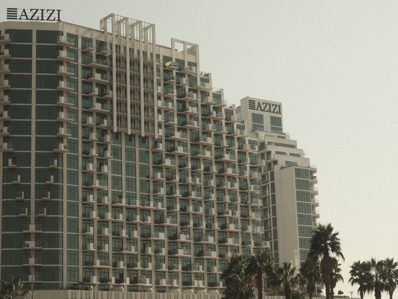 Modern high-rise buildings with balconies and palm trees in the foreground under a hazy sky.