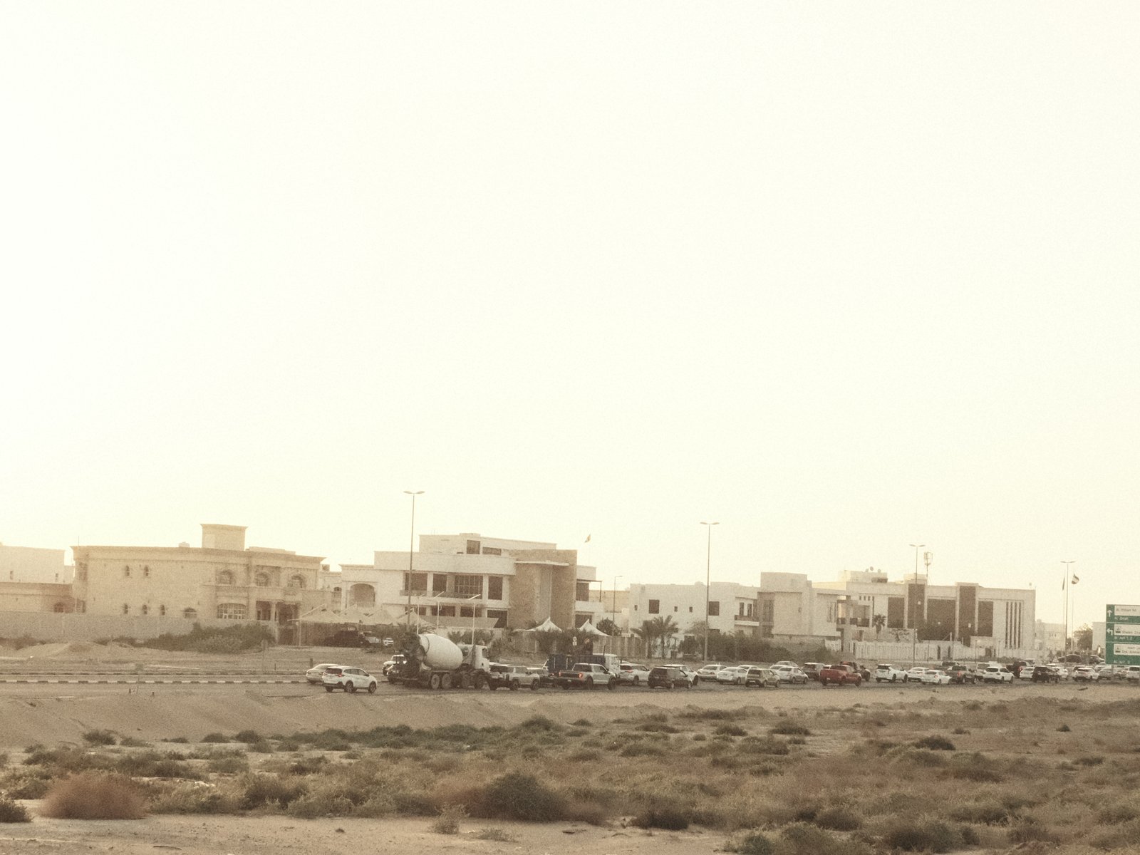 A distant view of a coastal town with beige buildings and parked vehicles under a hazy sky.