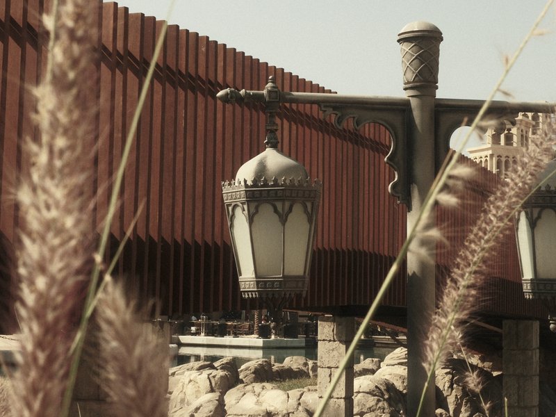 A vintage-style lantern hangs near a rustic fence, surrounded by tall grass in a sunny setting.
