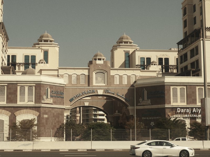 A vintage-style building with arches and domes, surrounded by a road and parked cars.