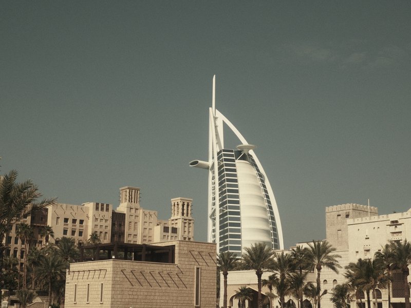 A modern skyscraper with a distinctive sail-like design amidst urban buildings and palm trees.