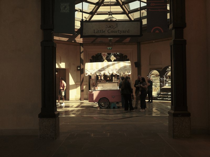 A bustling indoor market scene with a pink cart and people interacting under warm lighting.