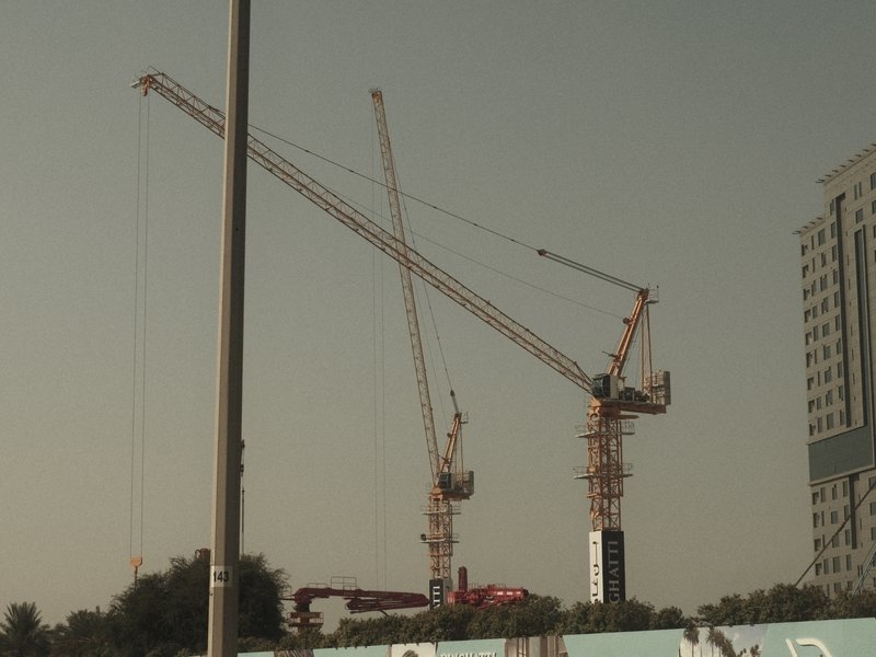 Two construction cranes against a clear sky near a building site.