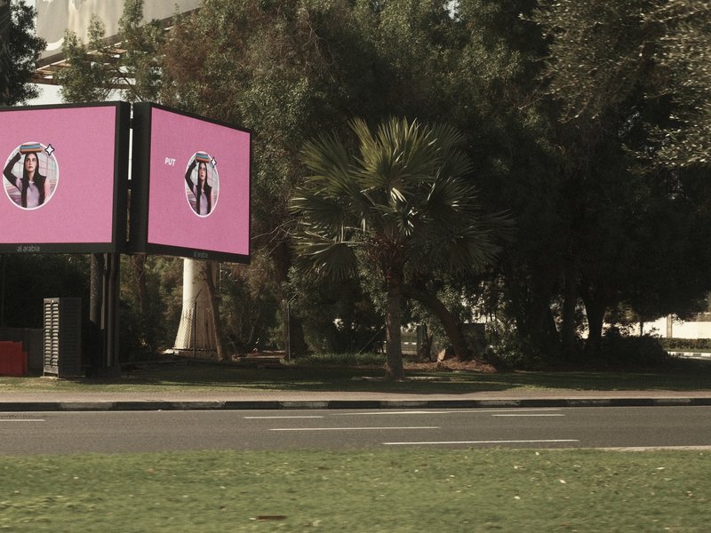 A pink billboard stands beside a green lawn with trees in the background under clear skies.