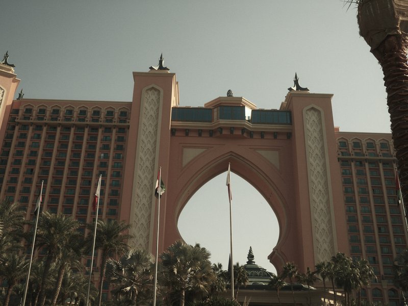 A grand archway of a hotel with palm trees in the foreground under a clear sky.