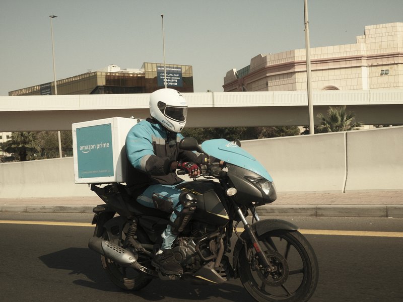 A delivery rider on a motorcycle wearing a helmet and blue uniform, riding on a city road.
