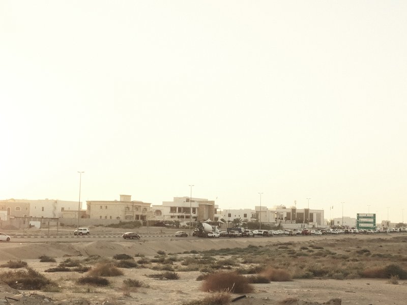 A distant view of a small coastal town with sandy terrain and light-colored buildings under a hazy sky.