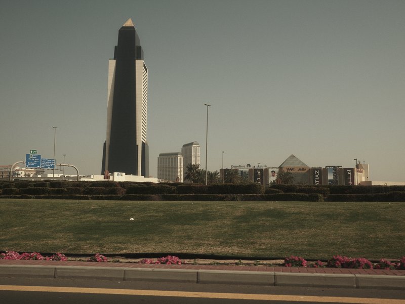 A tall modern skyscraper stands against a clear sky, with a grassy area in the foreground.