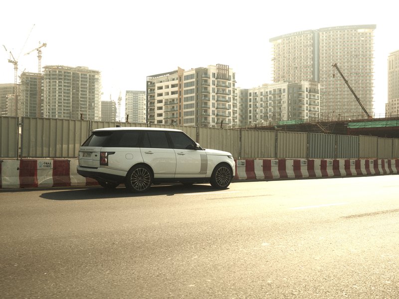 A white SUV parked on a city street with modern buildings in the background under bright sunlight.