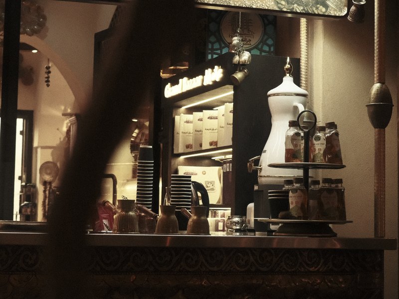 A cozy café interior with shelves of jars and a coffee machine, softly lit in warm tones.