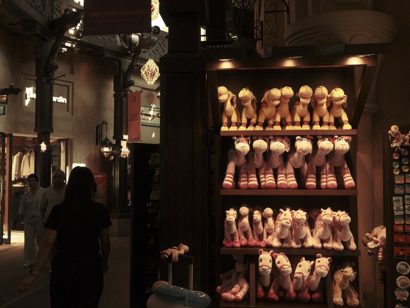 A display of plush toys in a store with warm lighting and a person walking by.