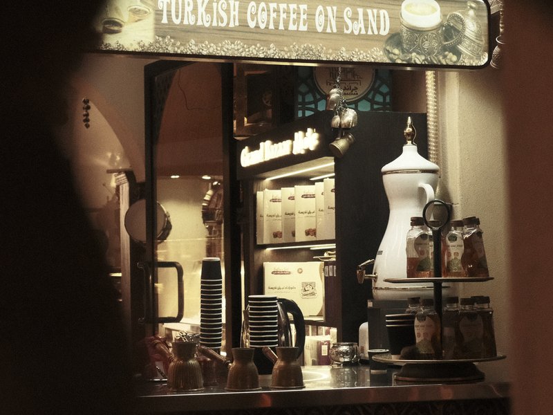 A cozy coffee shop interior featuring a sign for Turkish coffee on sand, with warm lighting.