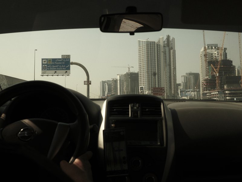 Interior view of a car with a driver's hand on the steering wheel, city skyline in the background.