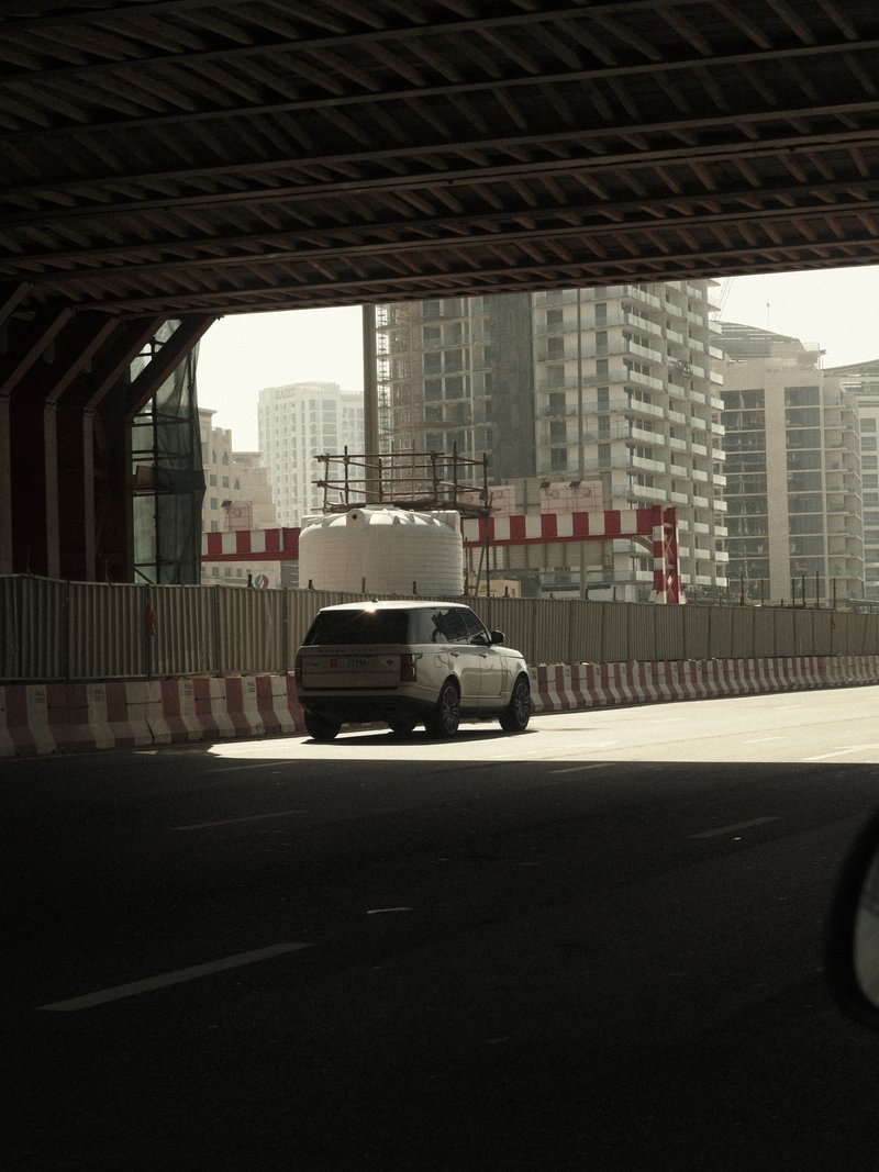 A car driving under a modern overpass with city buildings in the background.