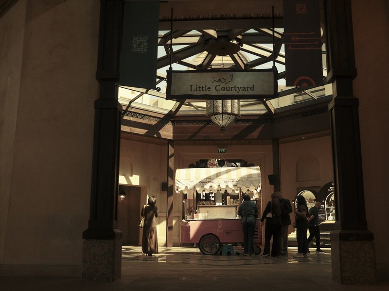 A bustling indoor market scene with a vintage ice cream cart and people gathered around.
