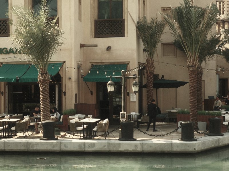 Outdoor dining area by a canal with palm trees and green awnings.