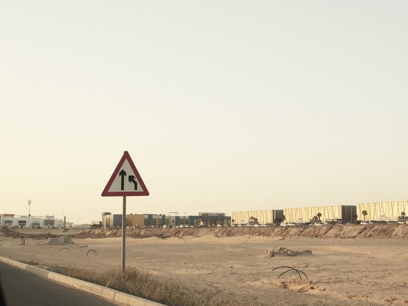 A road sign indicating construction ahead, with a barren landscape and distant construction vehicles.