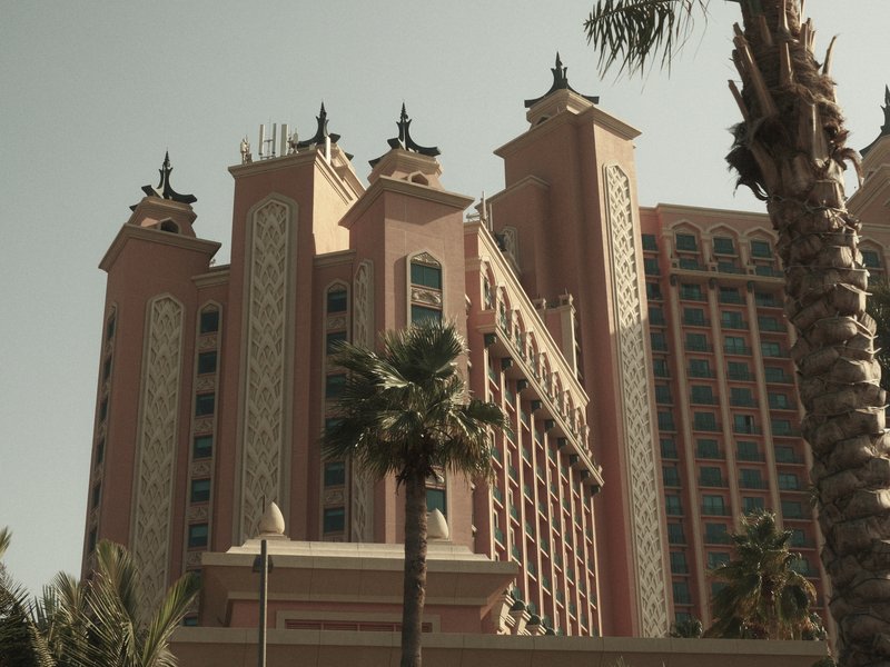 A tall hotel building with intricate architecture, surrounded by palm trees under a clear sky.