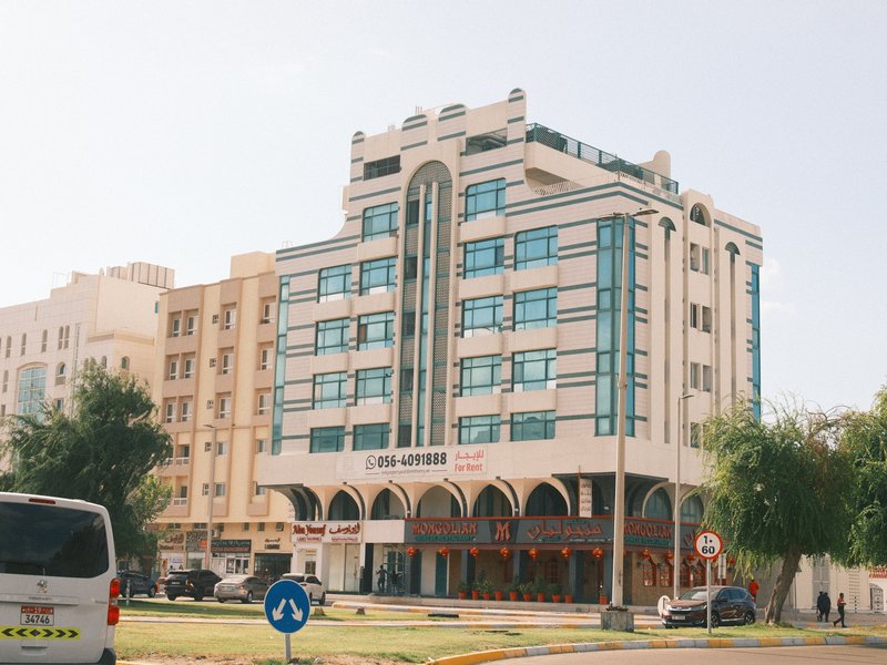 A modern building with large glass windows and an arched entrance, surrounded by greenery.