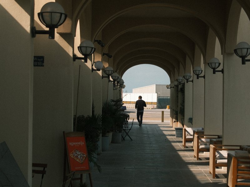 A person walking through an arched corridor with soft lighting and potted plants.