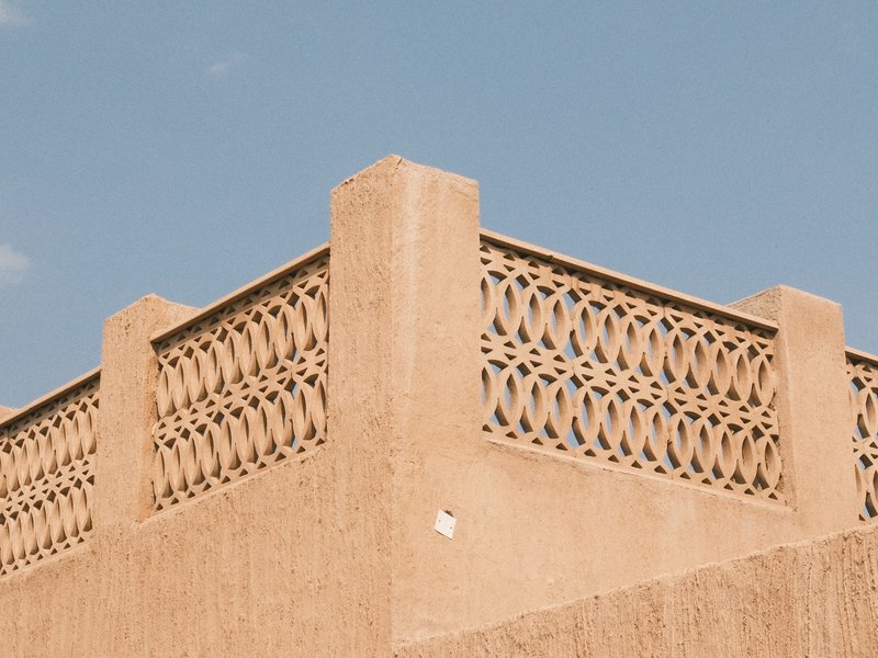 Close-up of a textured adobe wall with decorative latticework against a clear blue sky.