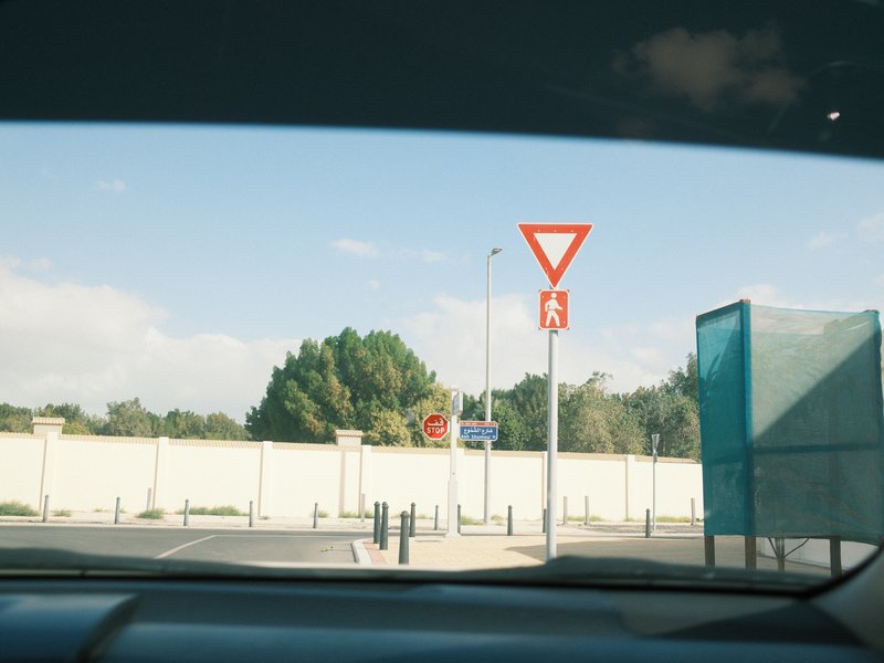View from inside a car showing a yield sign and a bus stop against a blue sky.