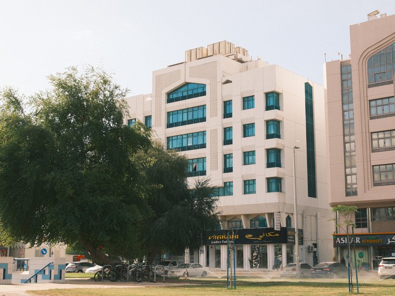 A modern building with large windows and a prominent tree in front, set in an urban environment.