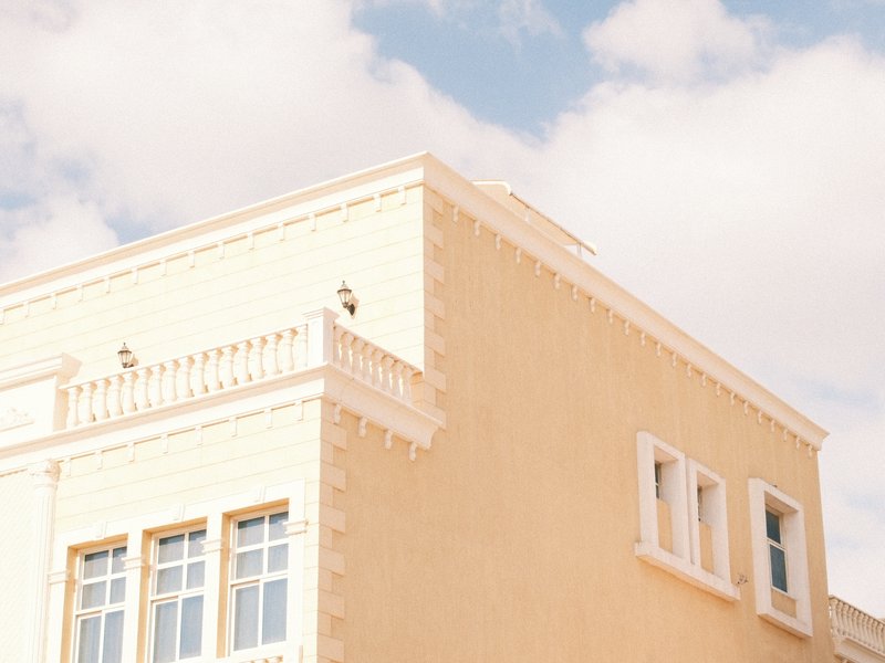 A corner of a light-colored building under a blue sky with fluffy clouds.