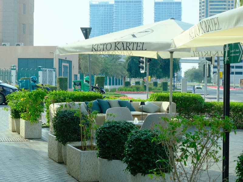 Outdoor seating area with green plants and umbrellas in an urban setting.