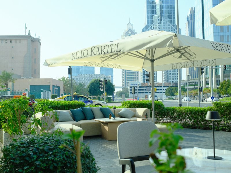 Outdoor cafe seating with umbrellas and city buildings in the background on a sunny day.