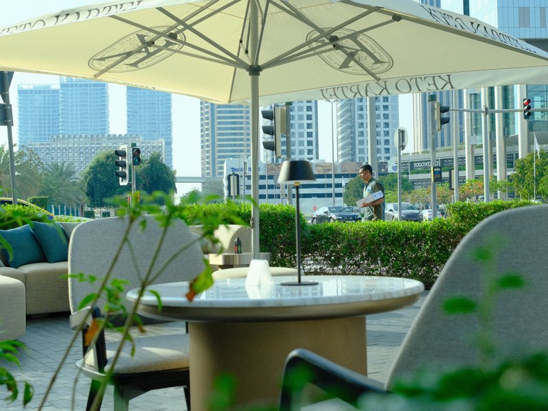 Outdoor café scene with a table and chairs, urban backdrop, and a person in the distance.