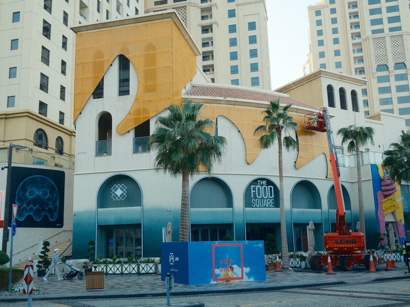 A colorful building with a unique design featuring palm trees and construction equipment nearby.