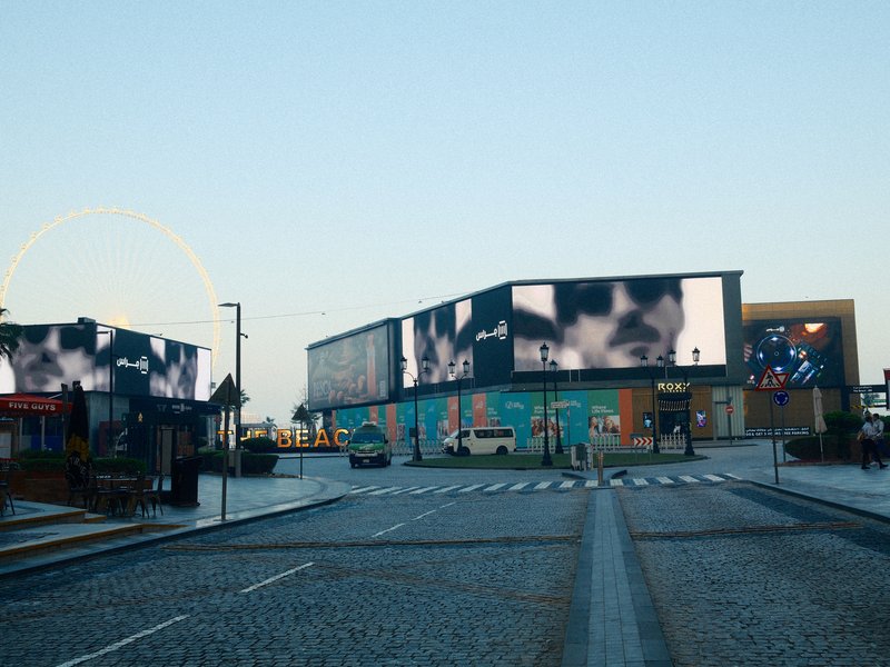 Urban scene featuring large digital billboards on buildings, with a clear sky and empty street.