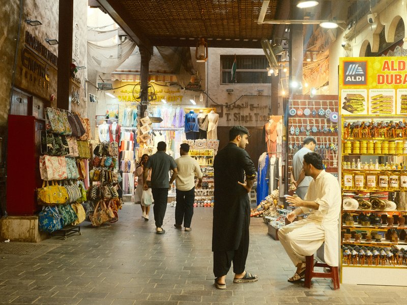 A bustling market scene with people walking among colorful stalls filled with goods.