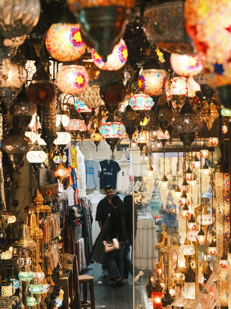 A vibrant market scene filled with colorful hanging lamps and decorations, with people browsing.