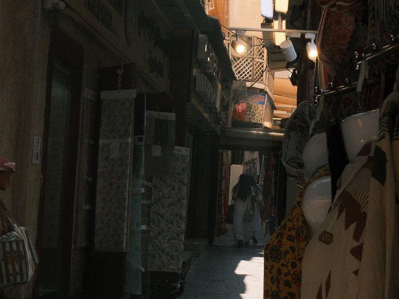 Narrow alleyway in a market with colorful textiles and pottery on display.