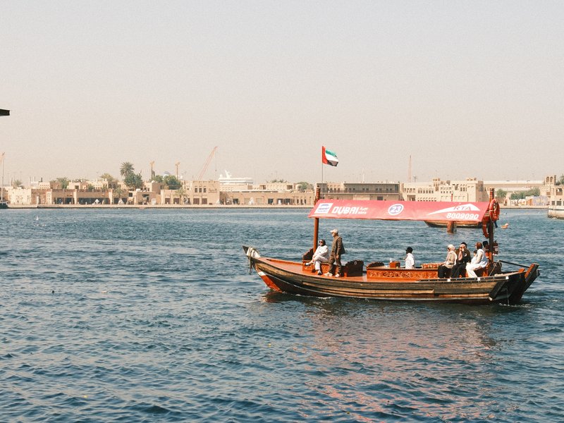A traditional wooden boat sailing on blue water with a city skyline in the background.