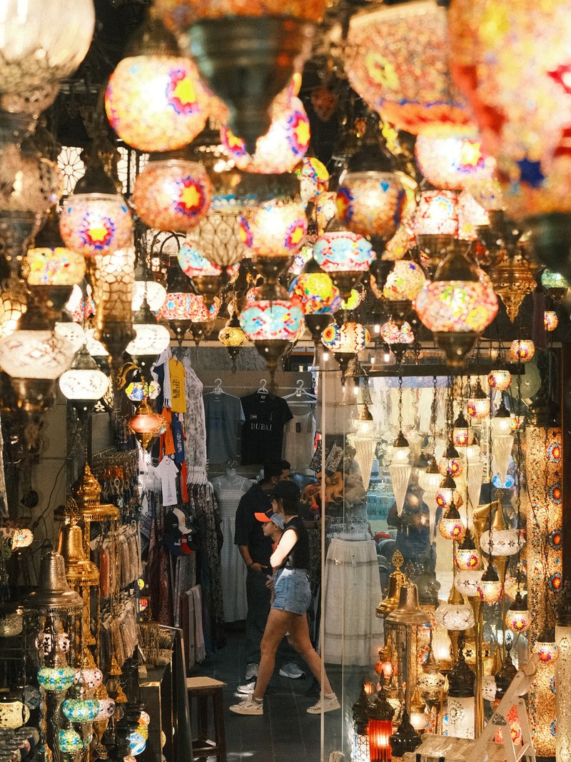 A vibrant market scene filled with colorful hanging lamps and decorative items, with a person walking through.