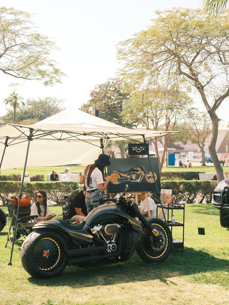 A black motorcycle parked under a tent at an outdoor event with people sitting and socializing.