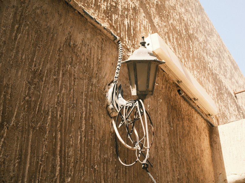A weathered wall with a hanging lamp and tangled wires, showcasing rustic textures and colors.