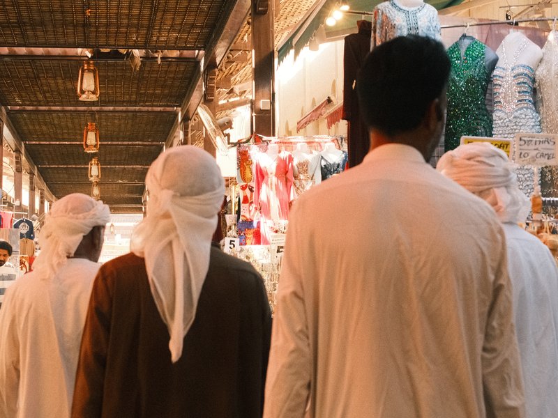 Group of men in traditional attire walking through a vibrant market with colorful stalls.