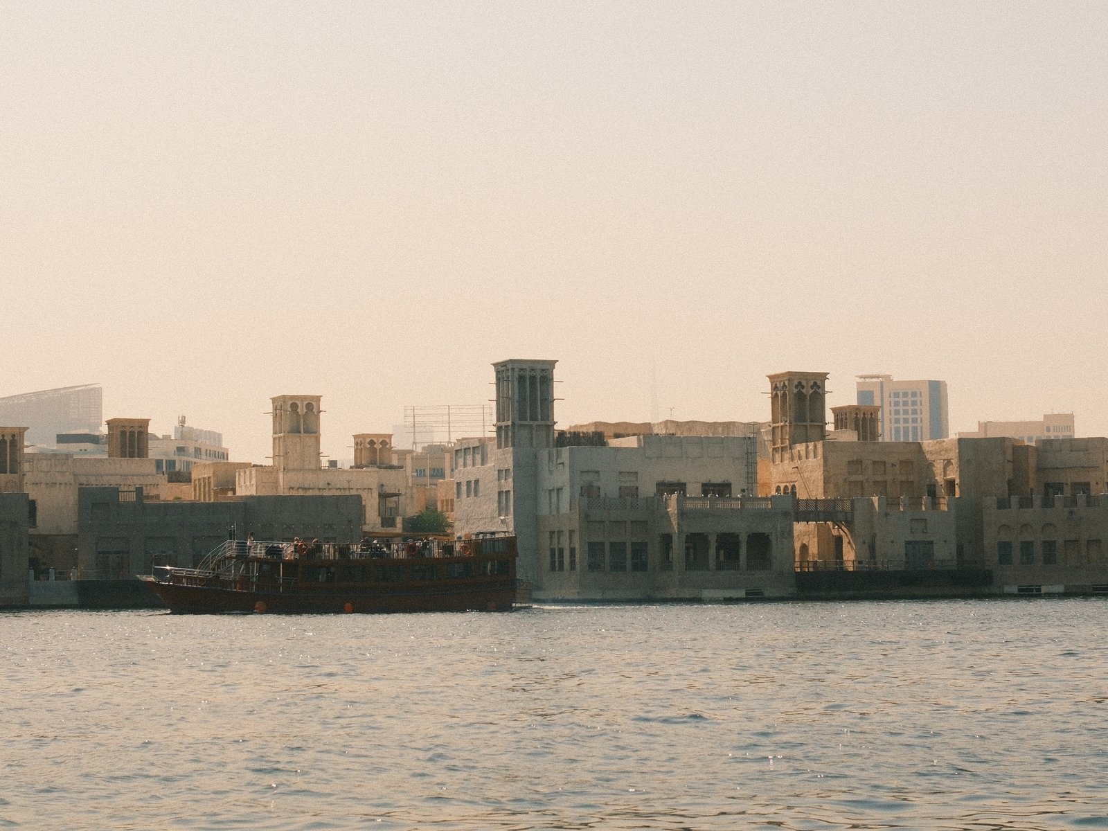 A view of traditional architecture along a waterfront with boats docked nearby under a hazy sky.
