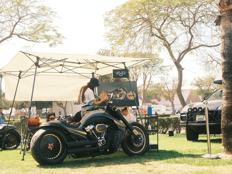 A custom motorcycle displayed under a tent at an outdoor event with trees in the background.